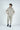 Clad in the Deerfield Hoodie Dark Khaki and matching joggers, a person with hands in their hoodie pockets sports dark blue sneakers and gazes sideways against a plain white background.
