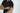 Someone wearing the Big League Notched V-Neck Short Sleeve Black tee adjusts their sleeve against a plain light background, preparing for a casual hangout. Their face is out of view in the image.