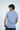 A man with wavy hair stands slightly turned in front of a plain white backdrop, wearing the light blue Big League Notched V-Neck Short Sleeve tee and black shorts.