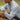 A man wearing a patterned long-sleeve golf shirt and white glove crouches on a grassy field. The shirt has a red logo on the sleeve, and he is wearing black shorts. His face is not fully visible.