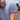 A person is wearing a blue polo shirt with small white palm tree patterns. The shirt has a navy blue collar and sleeve trim with white stripes. The person is outdoors, with a blurred view of grass and trees in the background.