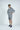 A person wearing a charcoal gray Deerfield Hoodie and matching shorts, crafted from super soft cotton with a cozy fleece interior, a white T-shirt, and navy sneakers stands with one hand in their pocket against a plain white background.