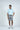 A man with short, dark hair stands against a plain background in a Jaxson Maximus West Palm Polo: Dolphin Tail Light Blue print, paired with gray shorts. He looks to the side, hand in his pocket, exuding effortless style in luxury performance fabric.