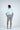 With their back to the camera, a person wears the West Palm Polo in Dolphin Tail Light Blue, luxury performance fabric short sleeves, paired with gray shorts and a blue belt. White sneakers finish the look against a simple white backdrop.