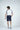 A man stands with his back to the camera wearing a Sanibel Polo White with Gray, luxury performance fabric navy shorts, and matching sneakers against a plain white background.