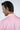 A man with dark hair is turned slightly to the side, wearing a pink collared West Palm Polo: Dolphin Tail Pink shirt made from luxury performance fabric. The shirts subtle patterns and text exude finesse, complementing the plain light background.