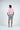 A man, facing away, wears the pink West Palm Polo: Dolphin Tail Pink, paired with gray shorts and white sneakers featuring black accents. The outfit exudes effortless charm against a plain white background.