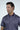 A man in a Sarasota Polo: Golf Girl Navy, made from luxury performance fabric, stands against a plain light background. Wearing the navy blue shirt with a white pattern and a button-up collar, his short dark hair and slight smile highlight the garments style and comfort.