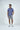 A man poses against a white background in the Panhandle Polo: Keys Coral Reef, a colorful Micro-Pique fabric short-sleeve shirt, paired with gray shorts and white sneakers. With one hand in his pocket and smiling, he glances slightly to the side.
