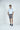 Against a plain white background, a man with short hair confidently models the West Palm Polo: Gingham Light Blue, luxury performance fabric shirt paired with gray shorts and dark sneakers.