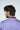 A person with wavy brown hair and a beard faces away from the camera, wearing the Sarasota Polo: Golf Cart Palm Purple. This luxury performance fabric shirt offers four-way stretch for comfort and style. The plain, light-colored background adds a tranquil vibe to the scene.