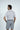 A dark-haired man with his back to the camera wears a West Palm Polo in white with navy stripes made from luxury performance fabric, paired with gray shorts. The simple, light-colored backdrop adds elegance to his casual ensemble.
