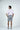 A man stands with his back to the camera wearing a gingham lilac West Palm Polo, gray shorts, and sneakers. His hands rest confidently on his hips against a plain white background.