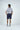 Man facing away, wearing the Sarasota Polo: Shark Attack White with luxury performance fabric and four-way stretch, navy shorts, and white sneakers, standing against a plain white background.