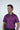 A man smiles, glancing sideways in a Sarasota Polo: Shark Attack Purple shirt. Made from luxury performance fabric, it ensures comfort and style. His dark hair stands out against the clean white background.